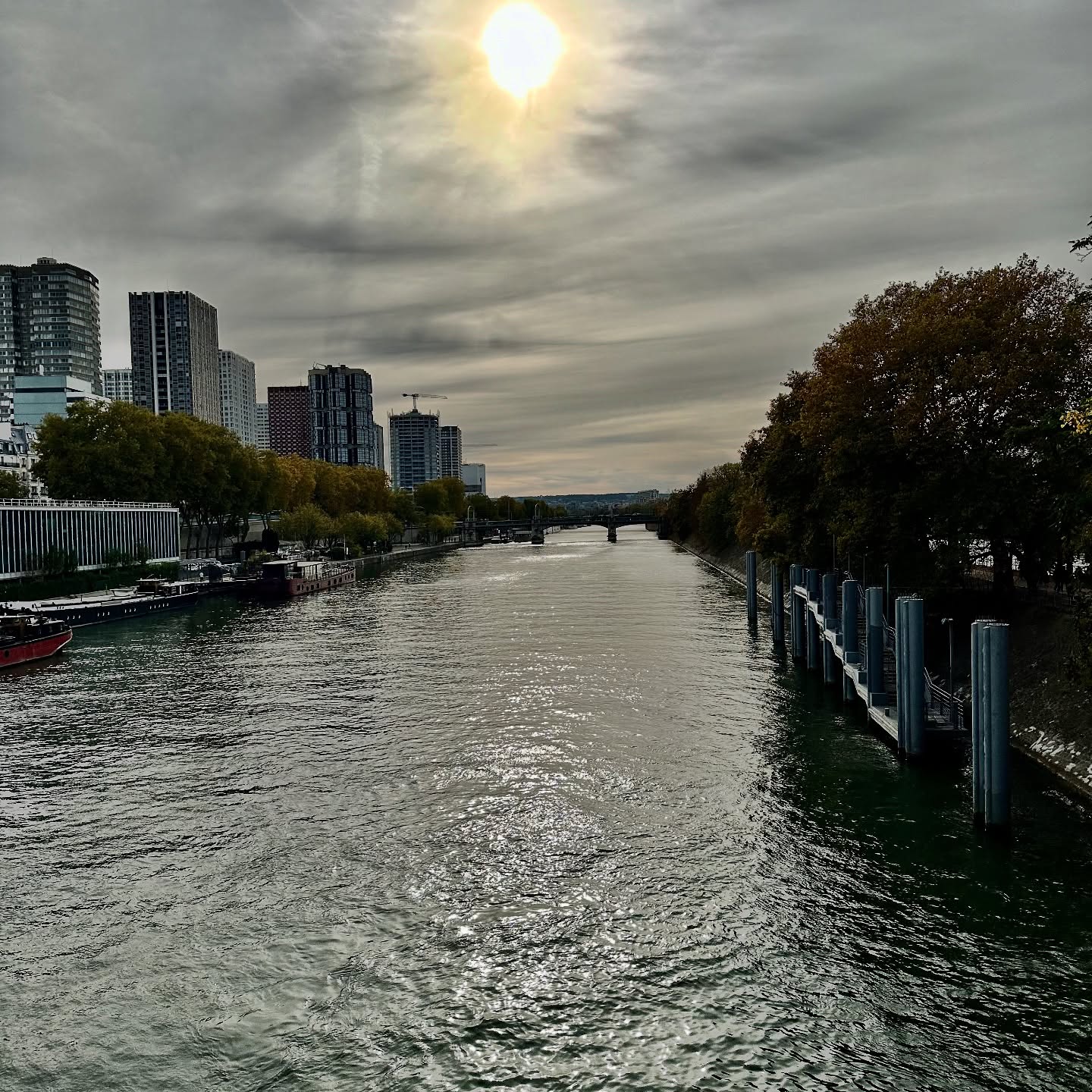 Reflets du soleil sur la Seine, avec des immeubles, des arbres et un pont au loin.